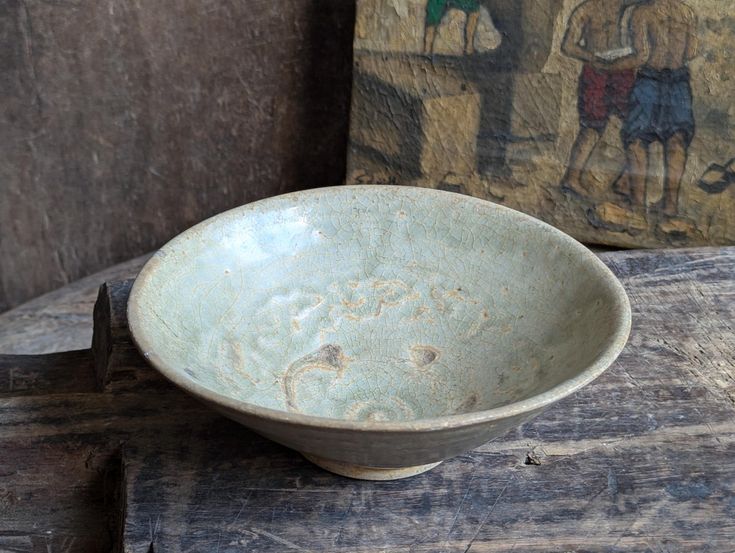 a blue bowl sitting on top of a wooden table next to a wall with paintings