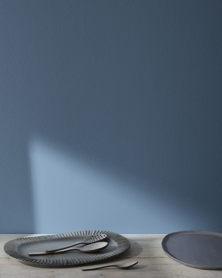 three plates and two spoons on a wooden table in front of a blue wall