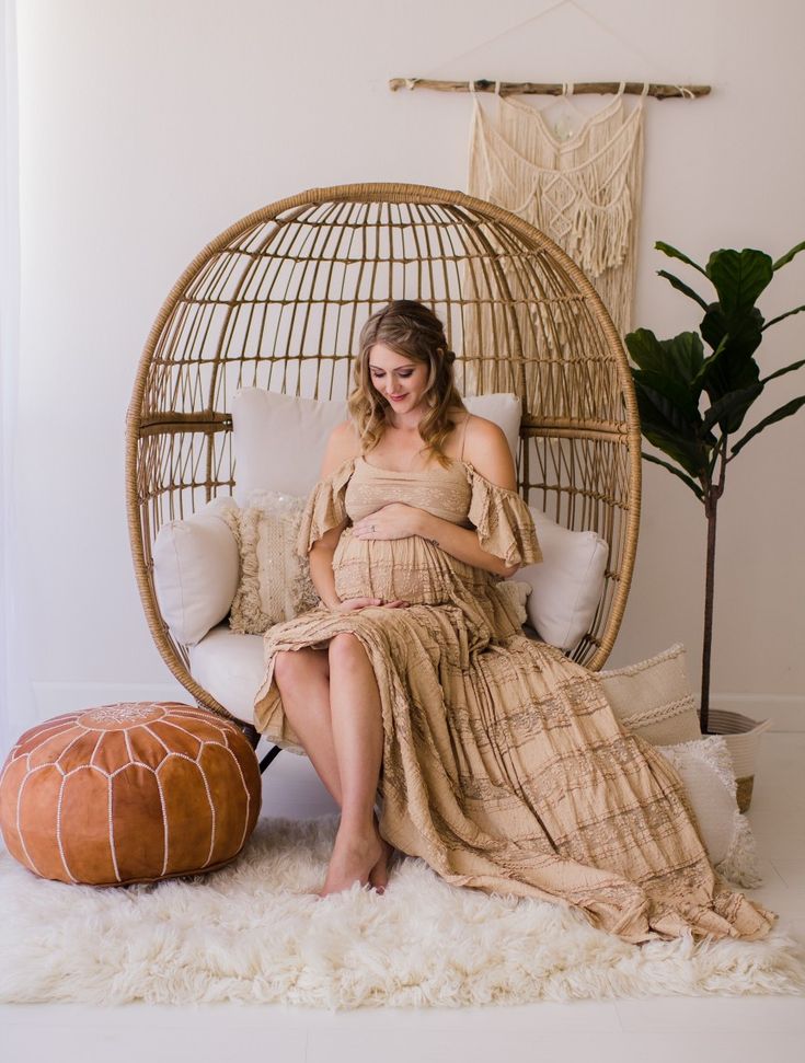 a woman in a dress sitting on a wicker chair next to a round ottoman