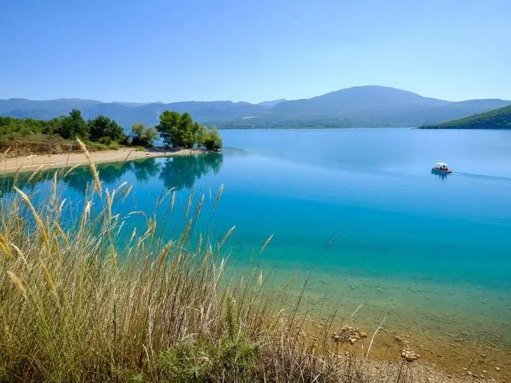 there is a boat that is in the water near some grass and trees on the shore