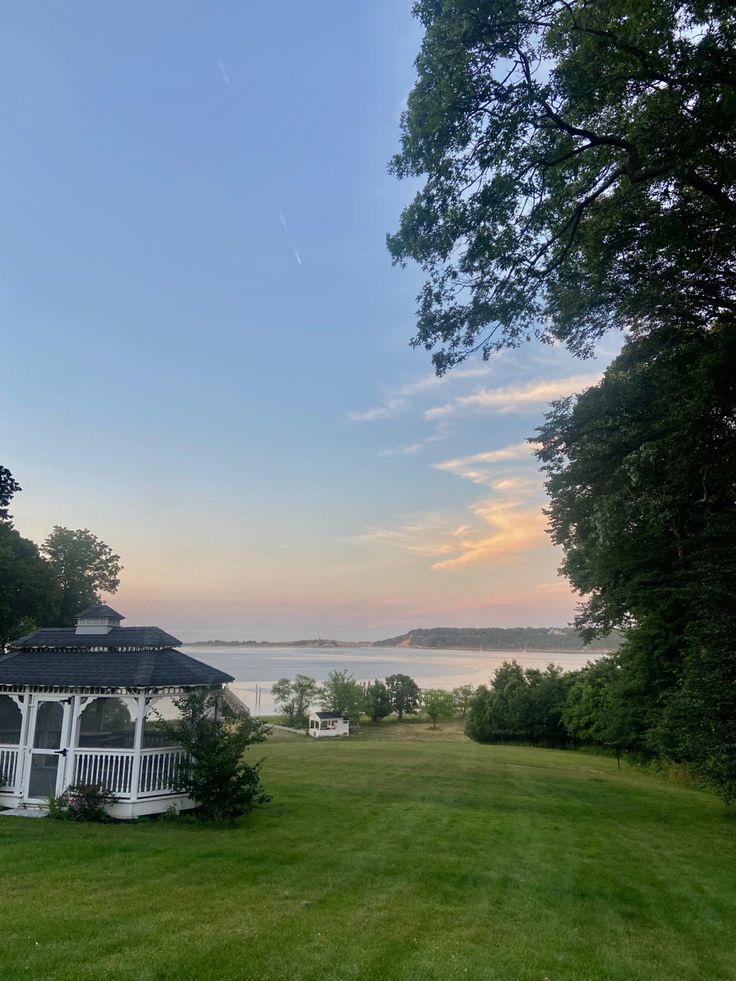 a gazebo sitting on top of a lush green field next to a lake at sunset