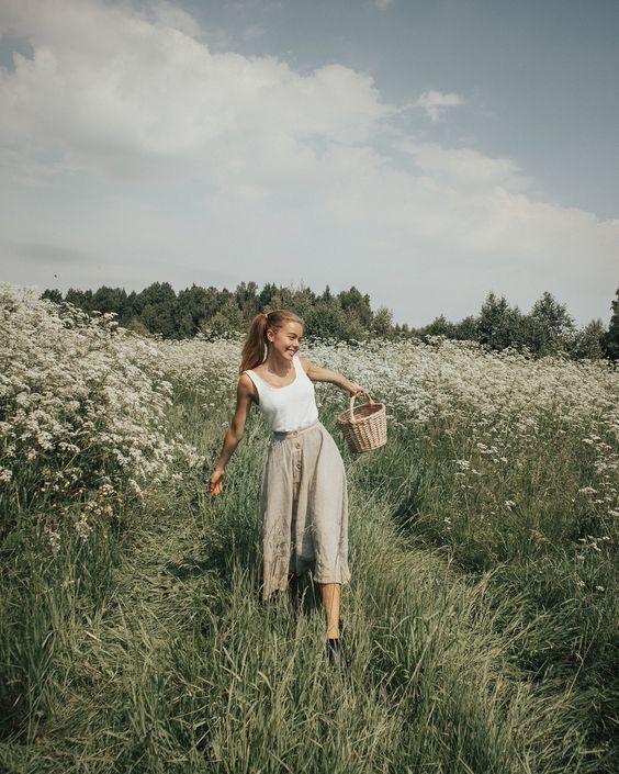 a woman is walking through the tall grass with a basket in her hand and smiling