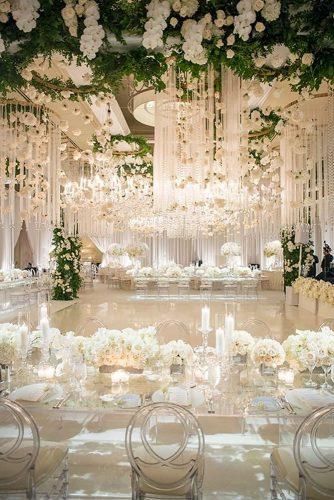 an elegant wedding reception with white flowers and chandeliers hanging from the ceiling over tables