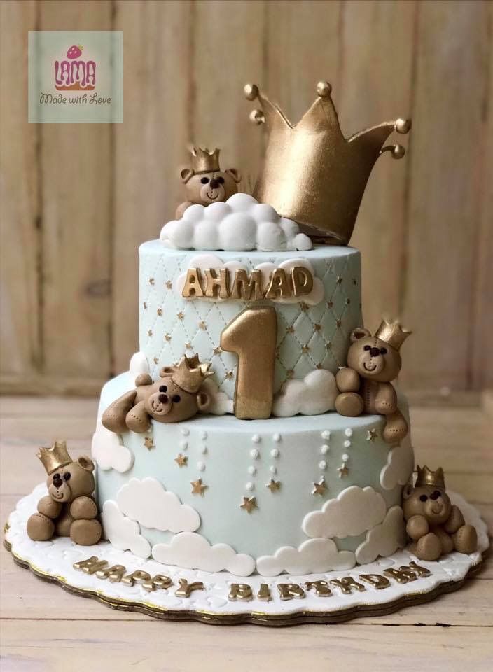 a blue and white cake with teddy bears on it's tiers, topped with a gold crown