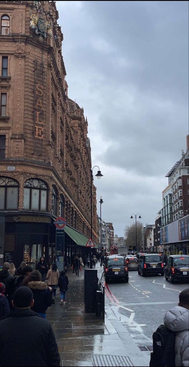 people are walking down the sidewalk in front of buildings on a rainy day with cars driving by