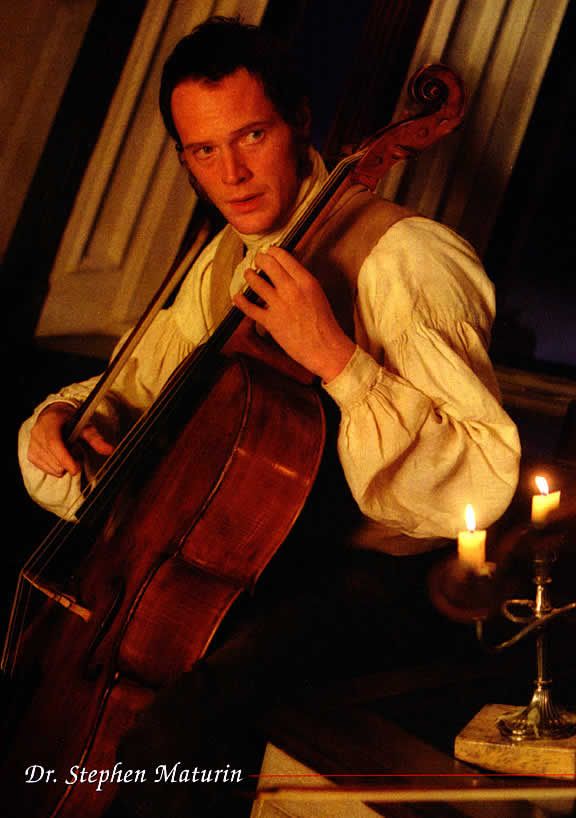 a man holding a cello in his right hand while sitting on a table with candles