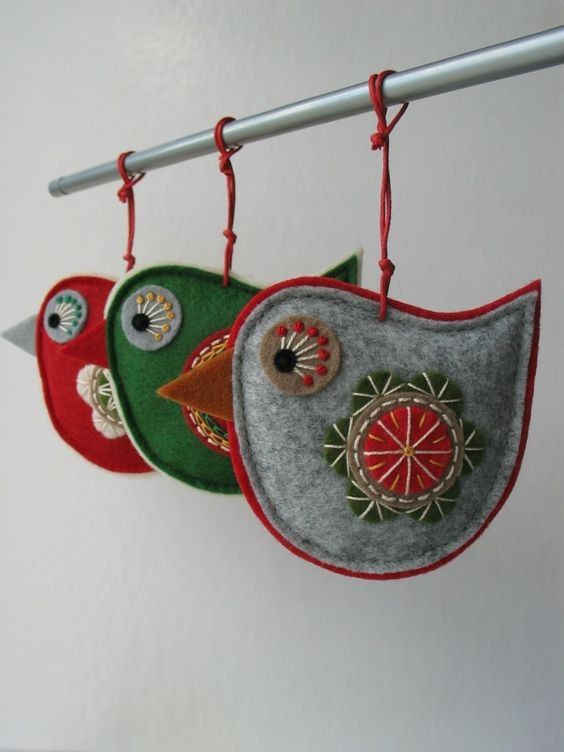 three felt birds hanging from hooks on a white wall with red and green trimmings