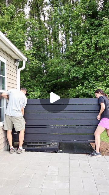 a man and woman standing next to each other near a wooden bench on the side of a house