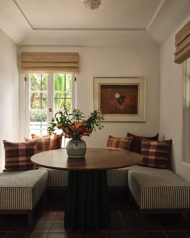 a room with a table, bench and flowers on the window sill in it