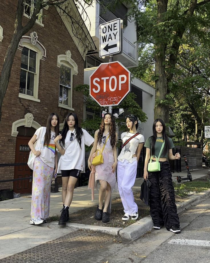 four young women standing in front of a stop sign on the side of a street