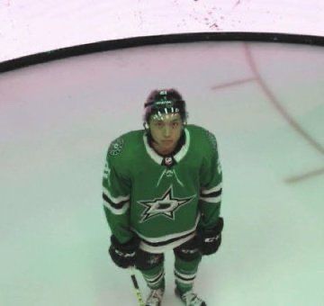 a hockey player in green jersey standing on the ice with his skates and gloves