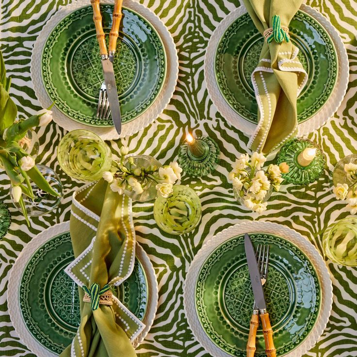 green and white plates with napkins, silverware and flowers on them are laid out