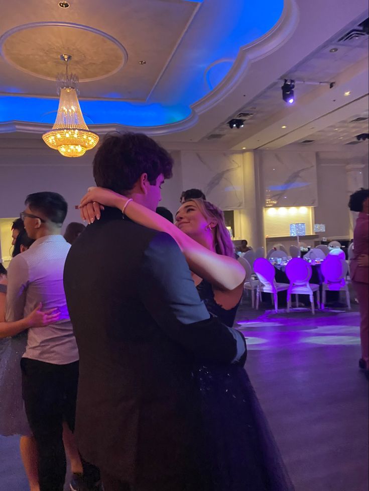 two people hugging each other while standing in a room with purple lighting on the ceiling