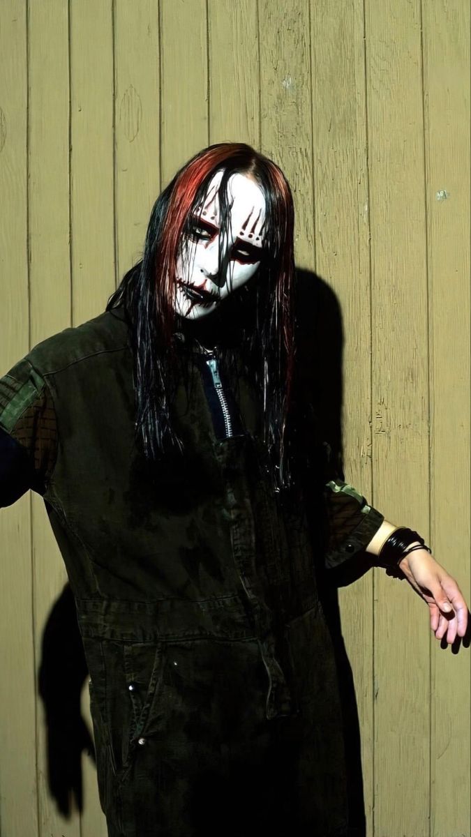 a man with blood on his face and long black hair standing in front of a wooden wall