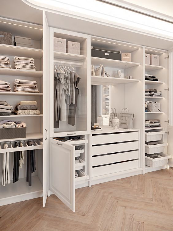 a walk in closet filled with lots of white drawers and shelves next to a wooden floor