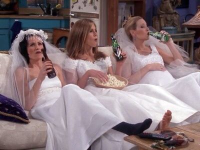 three women sitting on couches with one holding a bottle and the other wearing bridal gowns