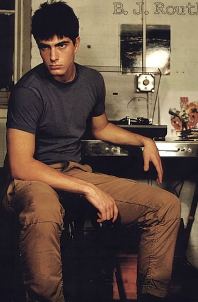 a young man sitting on top of a wooden chair in front of a desk with a lamp