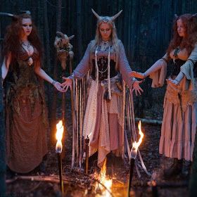 three women dressed as witches holding torches in the woods