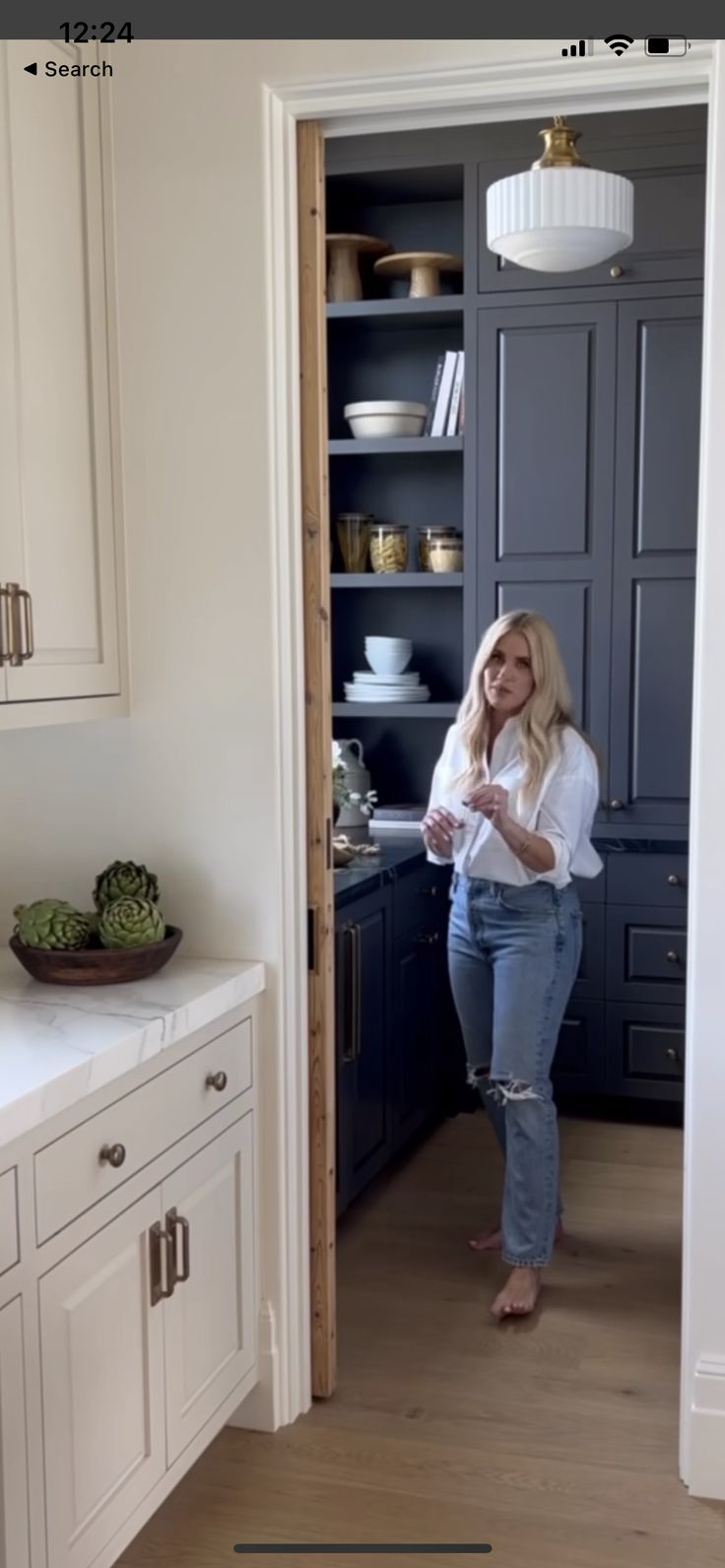 a woman is standing in the kitchen looking at her phone