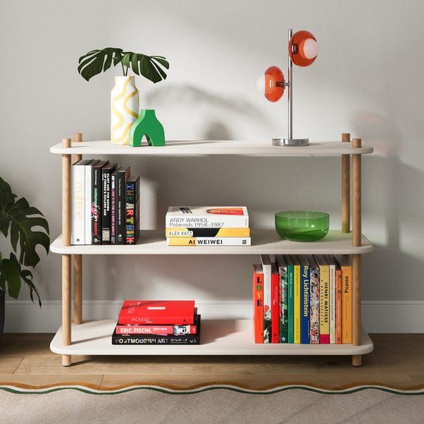 a book shelf with books, vases and other items on it in front of a white wall