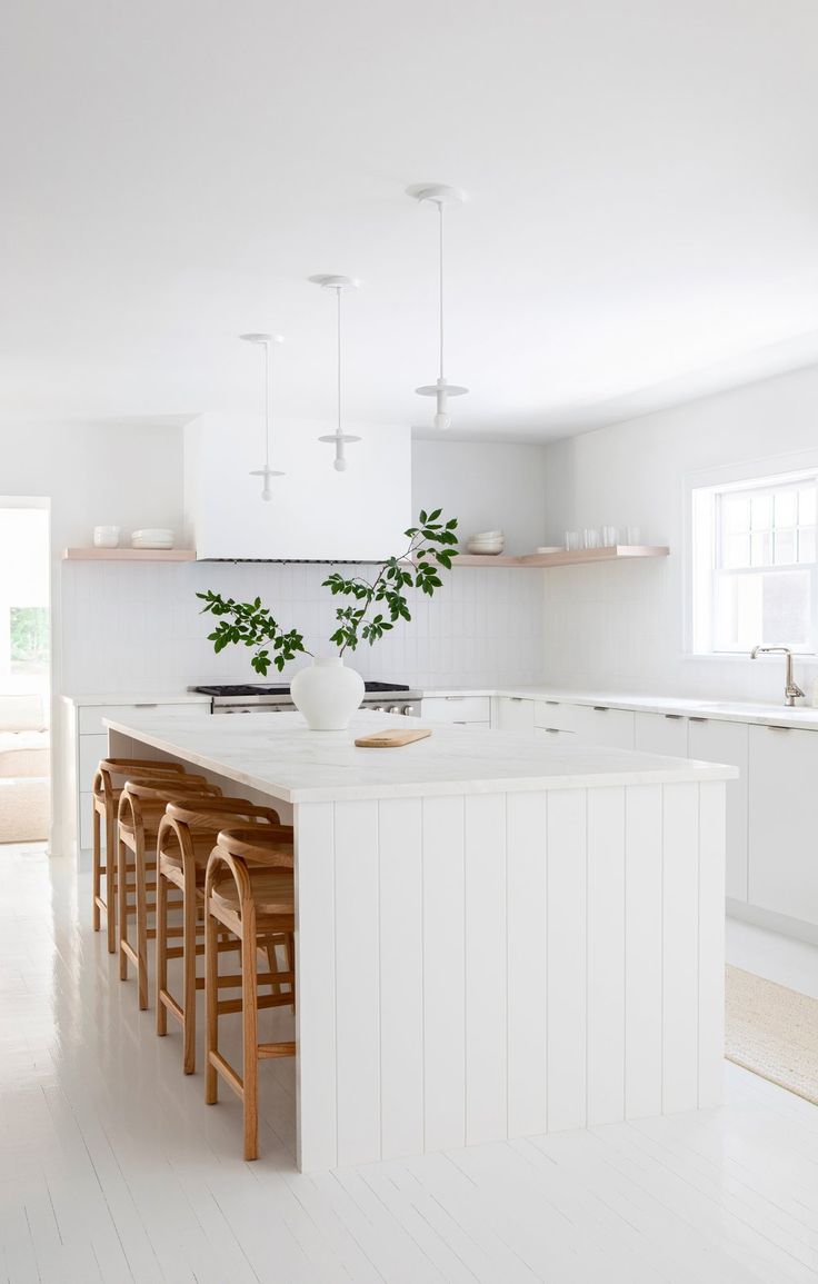 a white kitchen with wooden stools next to an island in the middle of the room