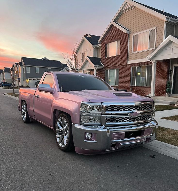 a pink truck parked on the side of a road next to some houses at sunset