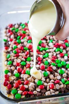 someone is pouring white sauce on some food in a glass dish filled with cereal and candy