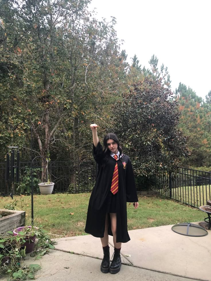 a woman dressed in a graduation gown and holding her fist up while standing on the sidewalk