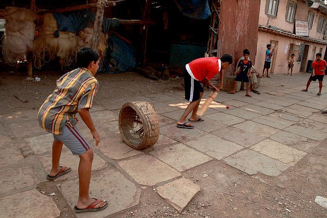 several children playing with an old tire on the ground in front of a building and some buildings