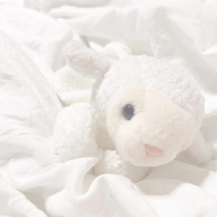 a white stuffed animal laying on top of a bed covered in white sheets and blankets