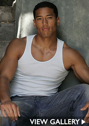 a man in white shirt and jeans sitting on the ground with his legs crossed looking at the camera