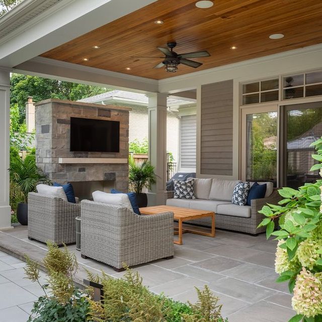 an outdoor living area with couches, tables and a television on top of a fireplace