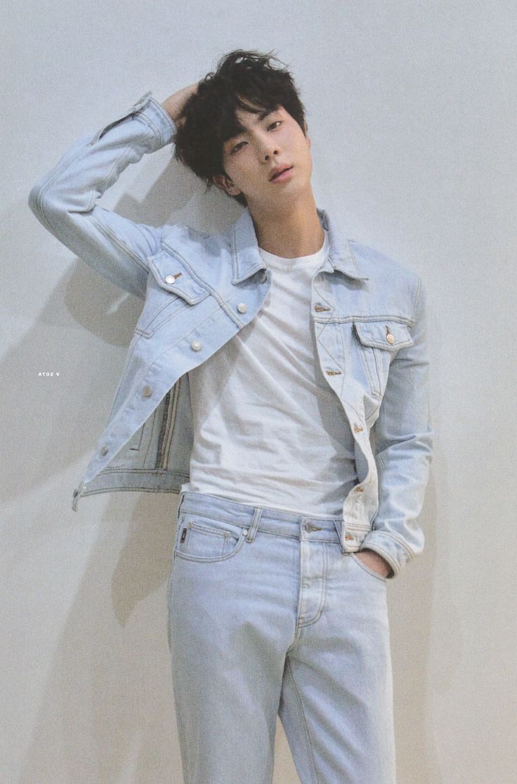 a young man leaning against a wall wearing jeans and a denim jacket with his hands on his head