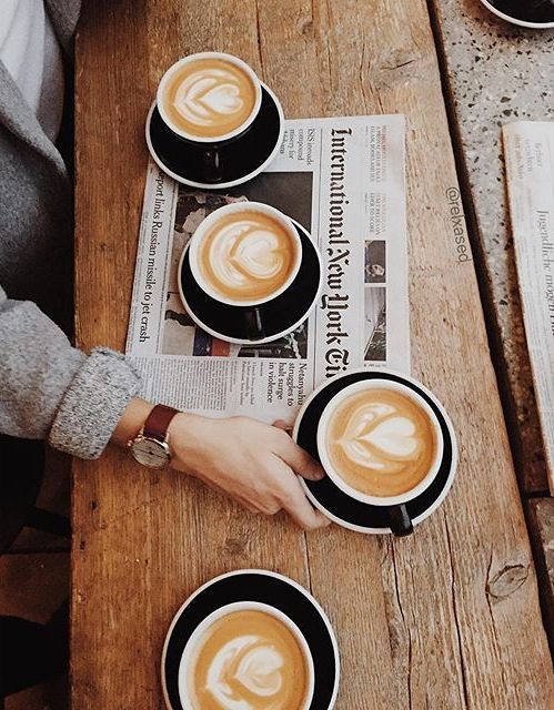 two people sitting at a table with cups of coffee in front of them and newspapers on the table