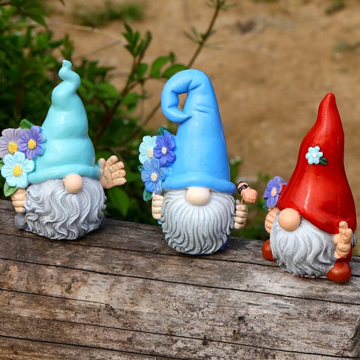 three gnome figurines sitting on top of a piece of wood