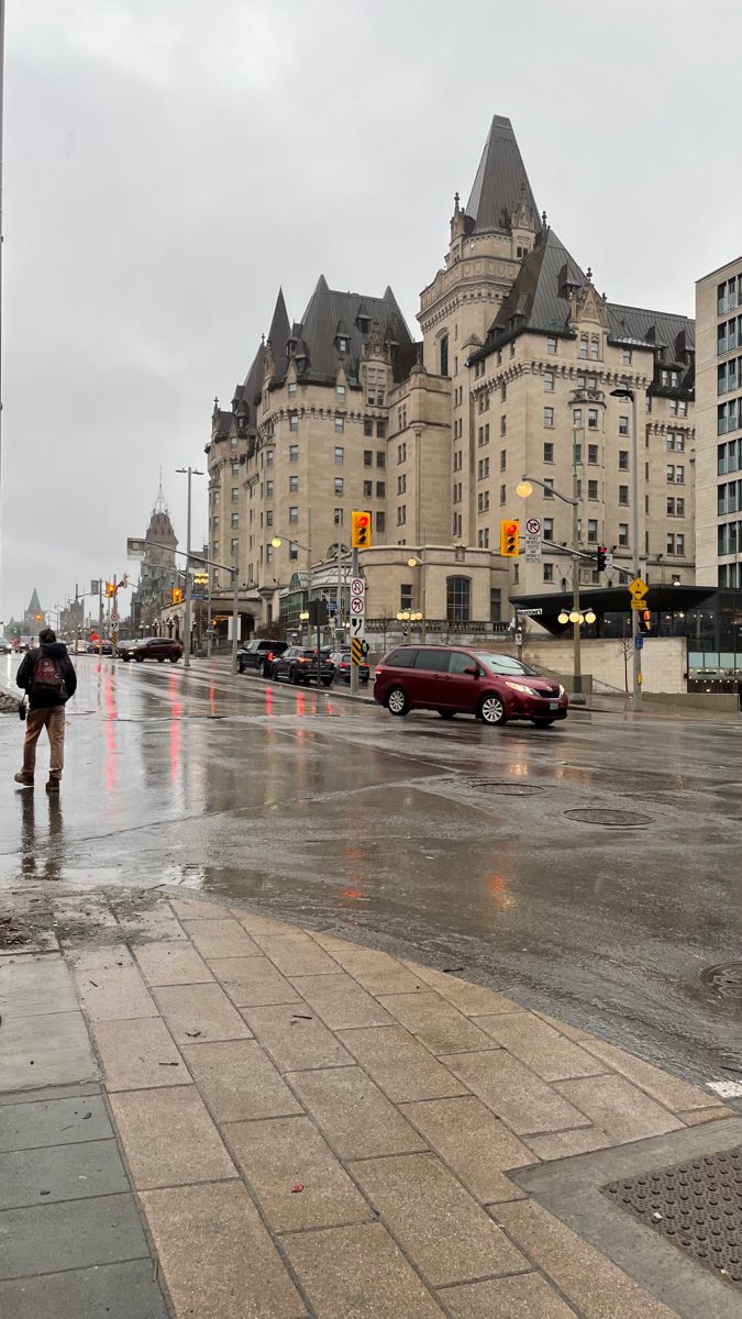 a wet city street with cars parked on the side and people walking in the rain