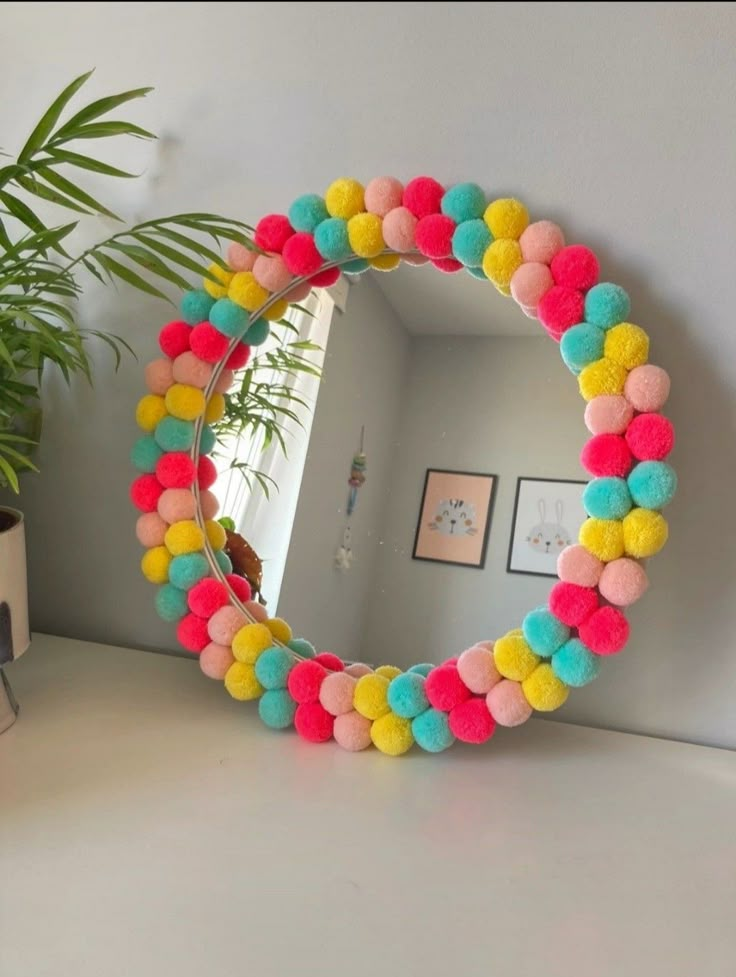 a mirror with pom - poms on it next to a potted plant