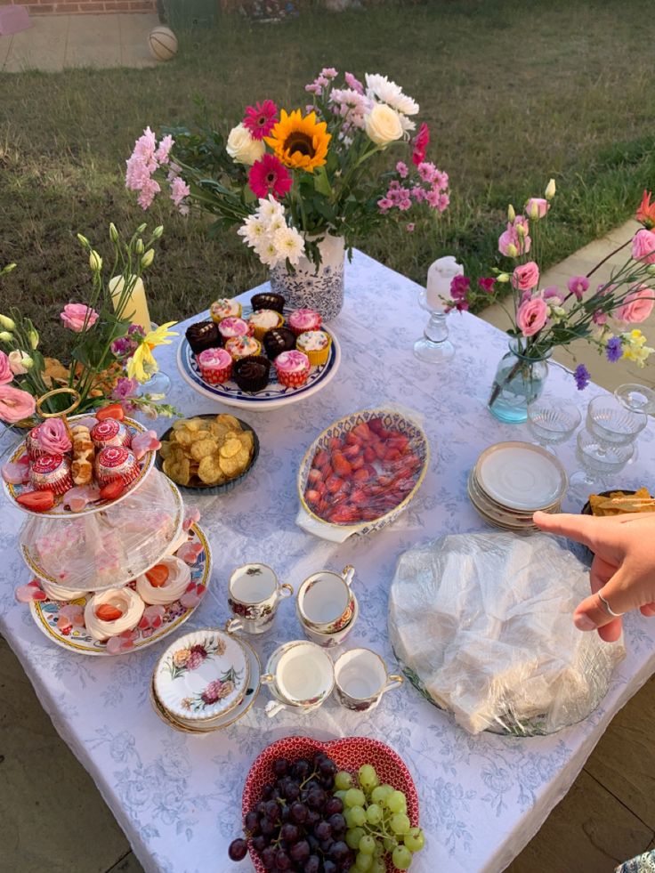 a table topped with plates and bowls filled with food next to flowers on top of a grass covered field