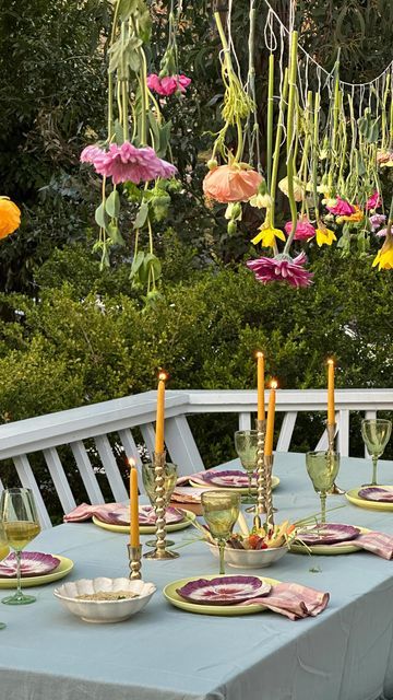 the table is set with plates, glasses and flowers hanging from the trees in the background