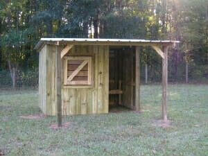 a small wooden outhouse sitting in the middle of a field next to some trees