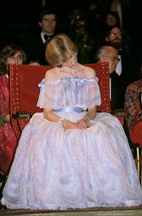 a woman in a white dress sitting on a red chair with other people behind her