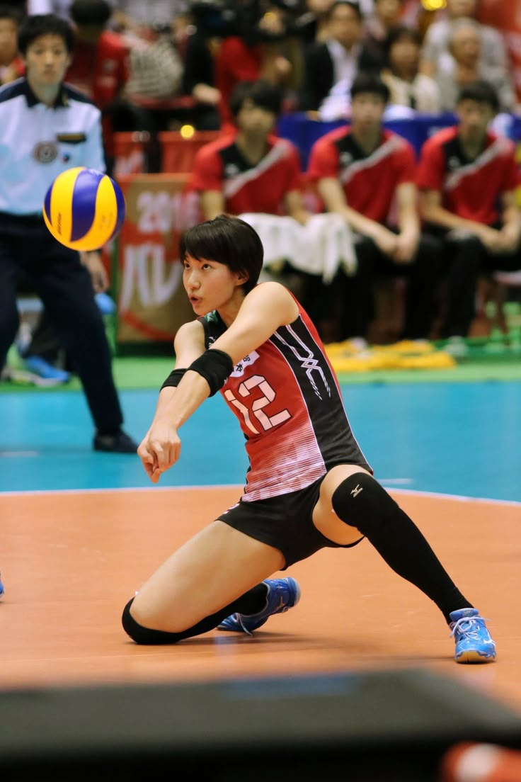 a woman in black and red uniform playing volleyball with people watching from the bleachers