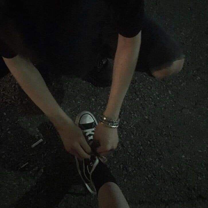 a person tying their shoelaces on the ground in the dark with no shoes