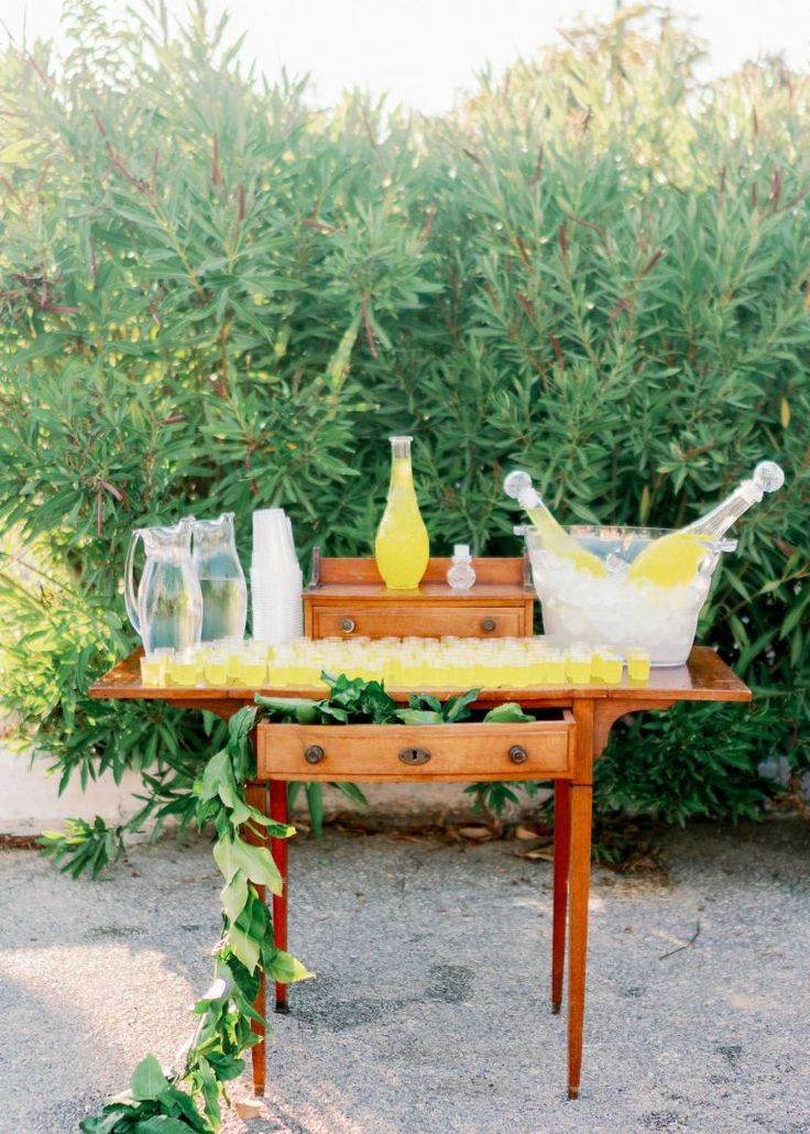 a wooden table topped with lots of bottles and vases next to plants on top of it