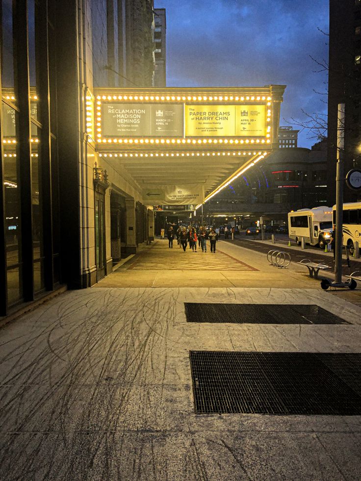 people are walking down the sidewalk in front of a building with lights on it's sides