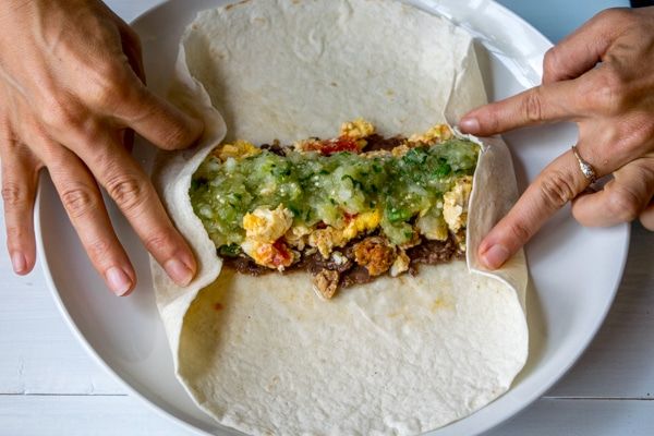 two hands reaching for an uncooked burrito on a plate