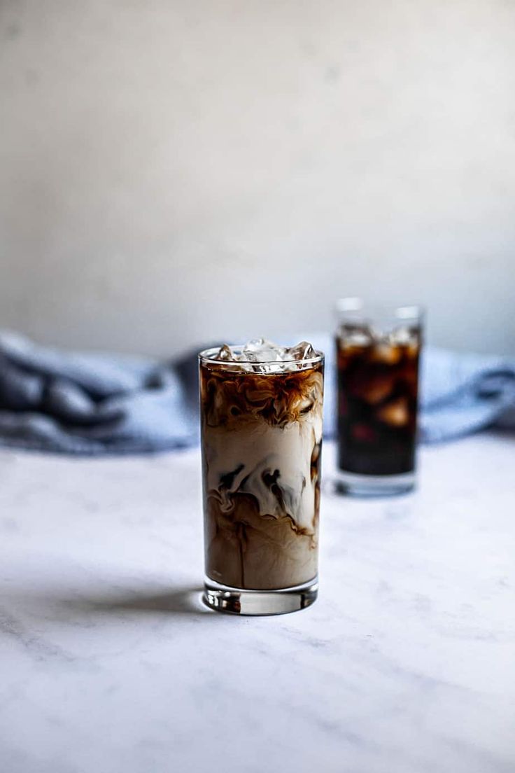 two glasses filled with drinks sitting on top of a white table next to each other