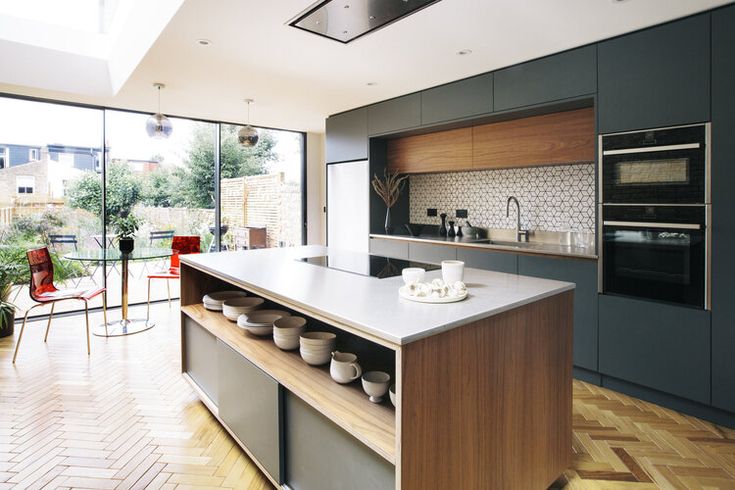 a modern kitchen with wooden floors and white counter tops, along with glass doors leading to an outdoor patio