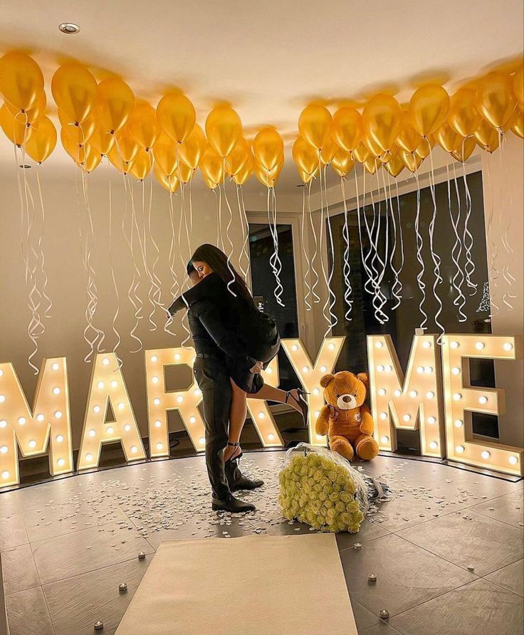 a woman standing next to a teddy bear in front of balloons