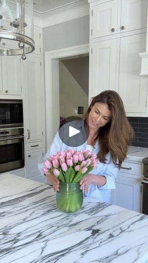 a woman arranging flowers in a vase on a kitchen counter